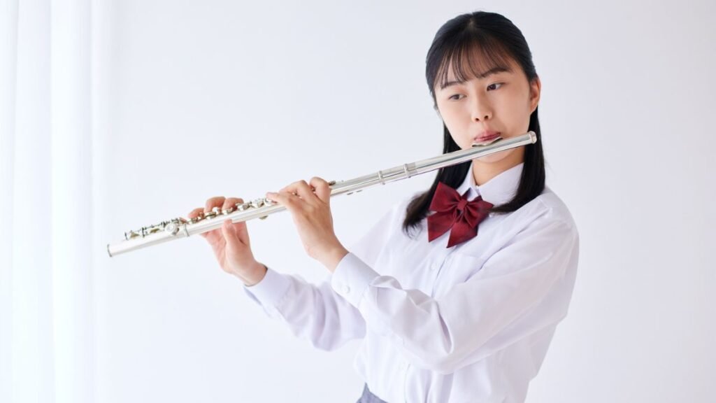 Egy fiatal lány furulyázik, kifejező arccal és elegáns öltözetben.