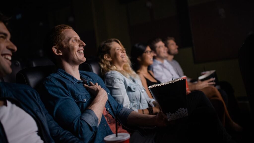 Öt fiatal ül a moziban, nevetve nézik a filmet, popcornnal a kezükben.