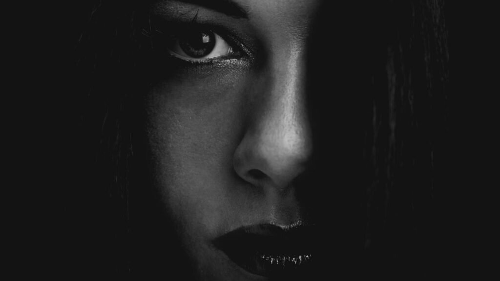 Egy női arc részlete sötét háttér előtt, titokzatos kifejezéssel.