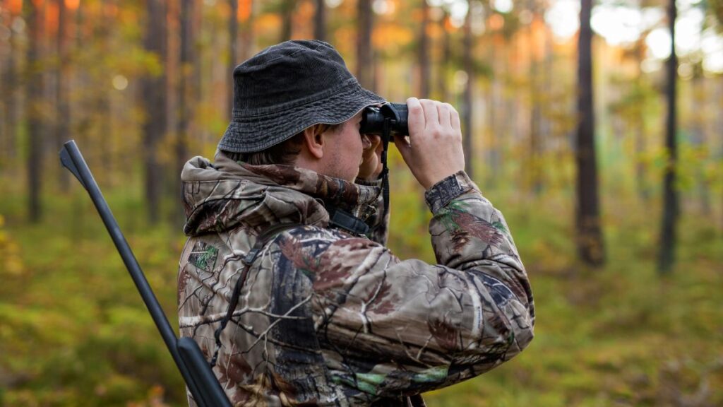 Vadászat az álomban jelentése Egy férfi vadászkabátban távcsővel figyeli a környező erdőt.