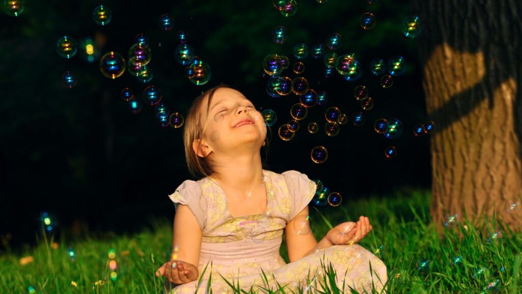 Csoda az álomban jelentése Egy boldog kislány ül a fűben, buborékokkal körülvéve, mosolyogva.