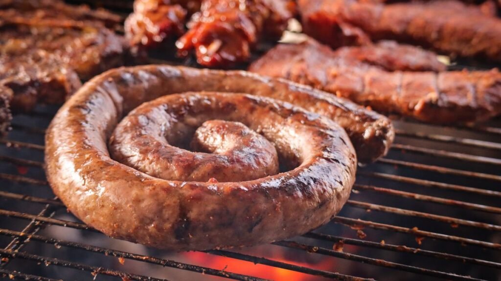 Grillezett kolbász spirál alakban, háttérben más húsételekkel.