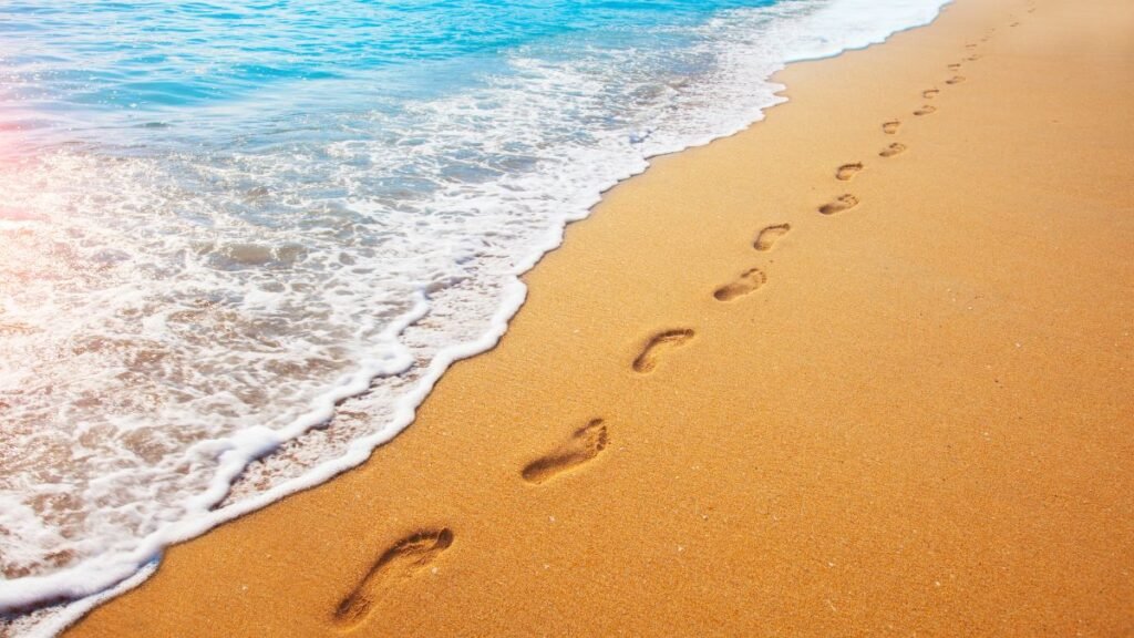 Homokos tengerparton lábnyomok, a víz part mentén hullámzik.