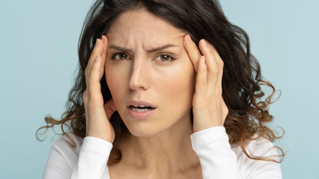 Egy nő, aki aggodalommal az arcán, a homlokát fogja, stresszes helyzetet jelezve.