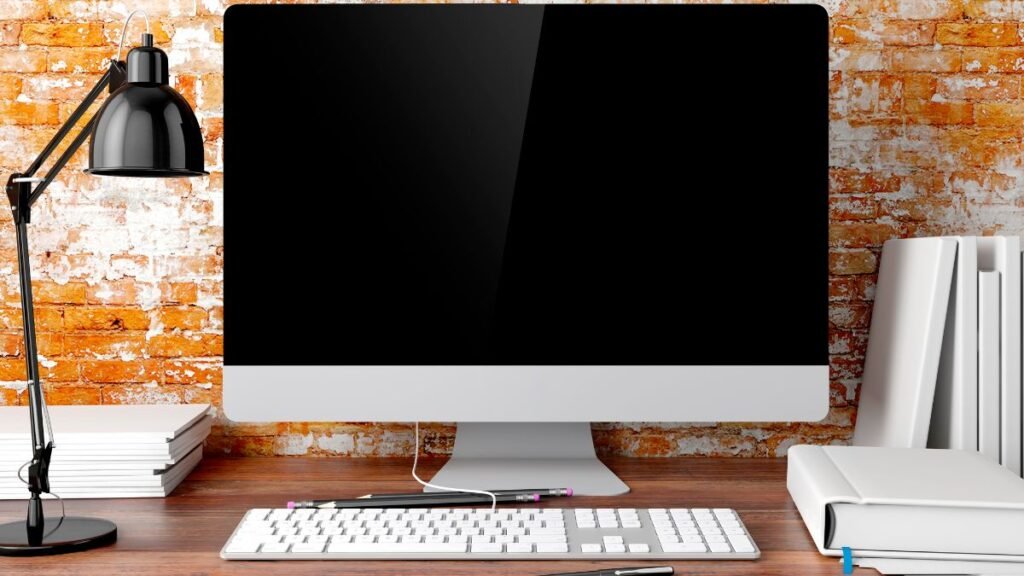 Egy modern számítógép asztalon, mellette könyvek és lámpa.