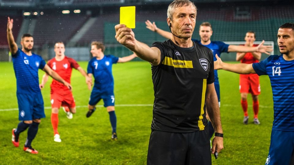 A játékvezető sárga lapot mutat a focimeccsen, a játékosok reagálnak.