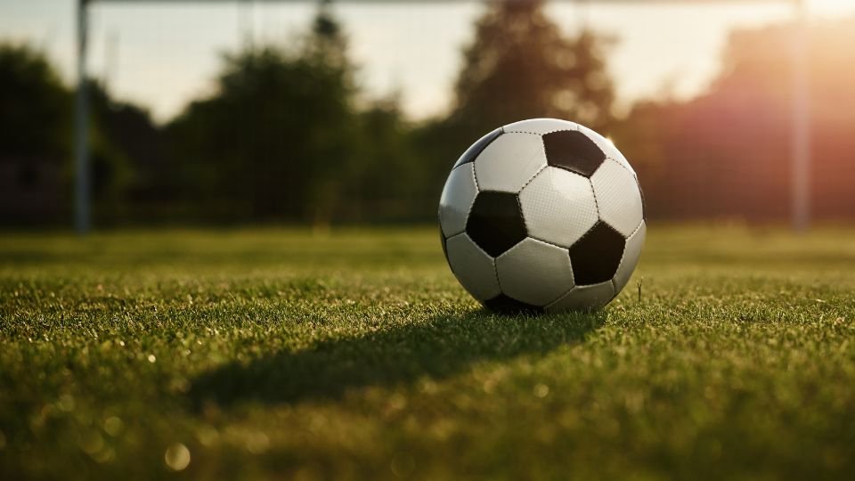 Egy focilabda fekszik a zöld fűben, háttérben a kapu látható.