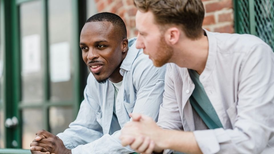 Két férfi beszélget egy kávézó teraszán, mély gondolatokkal.