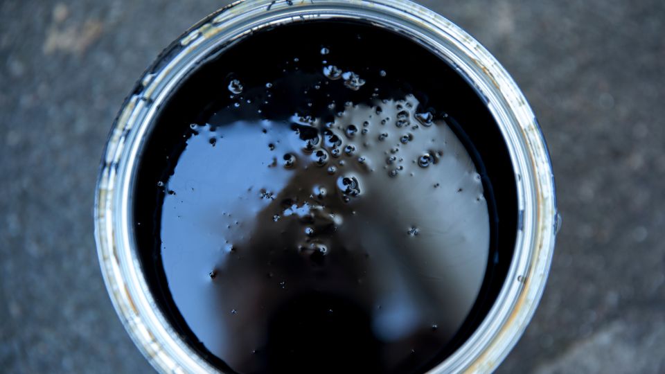Egy nyitott vödör kátrányról, sötét folyadékkal, buborékokkal a felszínen.