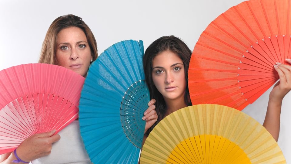 Két nő színes legyezőkkel a kezükben, hűvös és elegáns megjelenéssel.