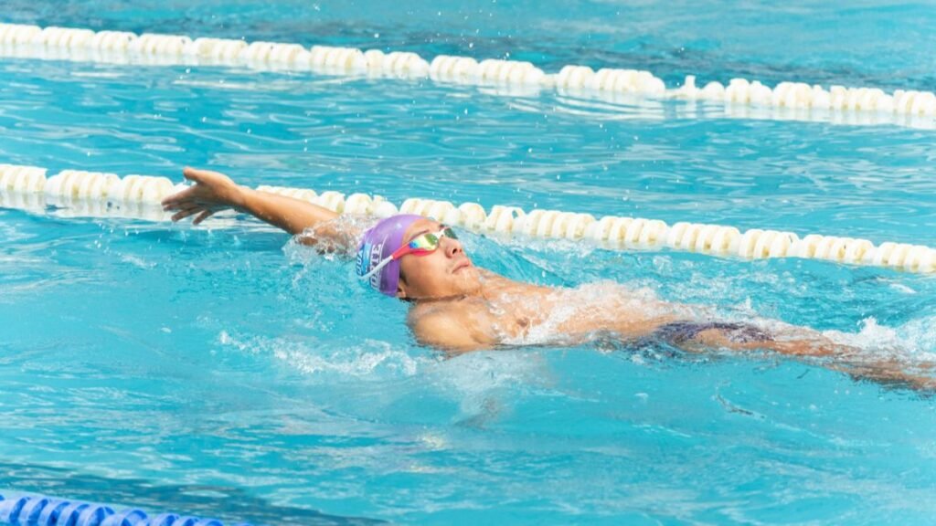 Egy sportoló hátúszás közben, vízben, nyugodt arckifejezéssel.