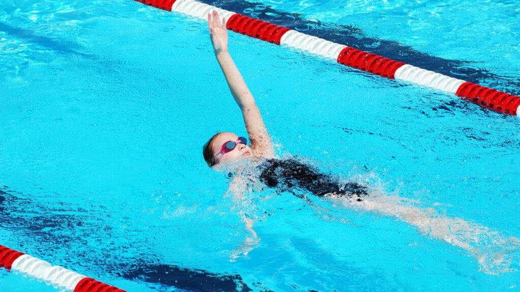 Egy fiatal lány hátúszás közben a medencében, víz alatti buborékokkal.