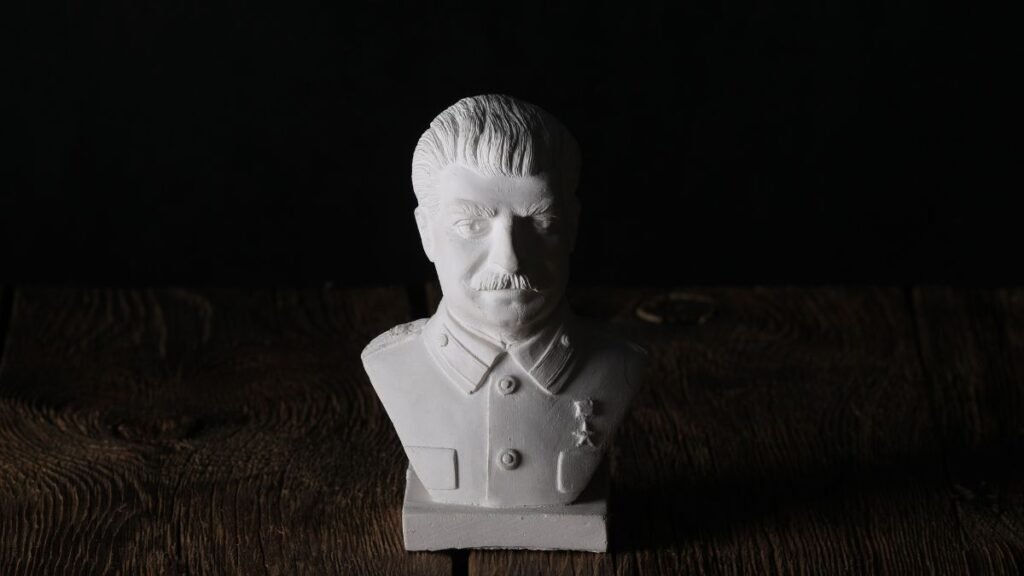 Egy fehér mellszobor, amely egy diktátorra emlékeztet, sötét háttér előtt.