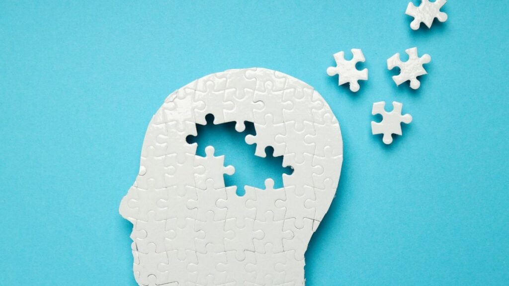 Egy fehér puzzle darabokból készült fej, amelyből hiányzik egy rész, kék háttér előtt.