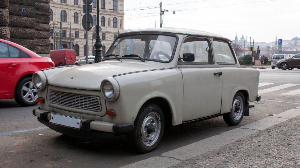 Egy régi Trabant autó áll egy városi utcán, a háttérben modern épületekkel.