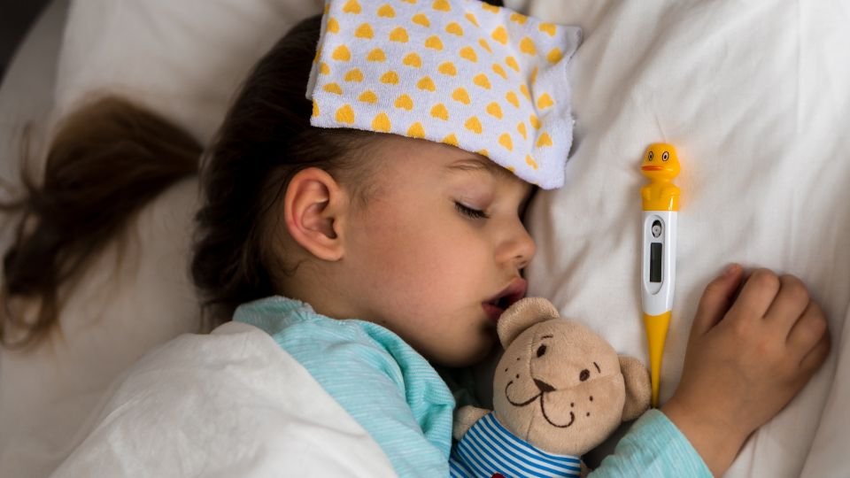 Beteg gyerek alszik, lázcsillapítóval és plüssmacival a kezében.