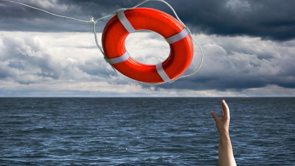 Egy mentőgyűrű lóg a víz felett, miközben egy kéz nyúlik utána.
