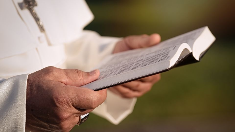 A pápa kezében egy nyitott Biblia, amely a hit és a spirituális útkeresés szimbóluma.