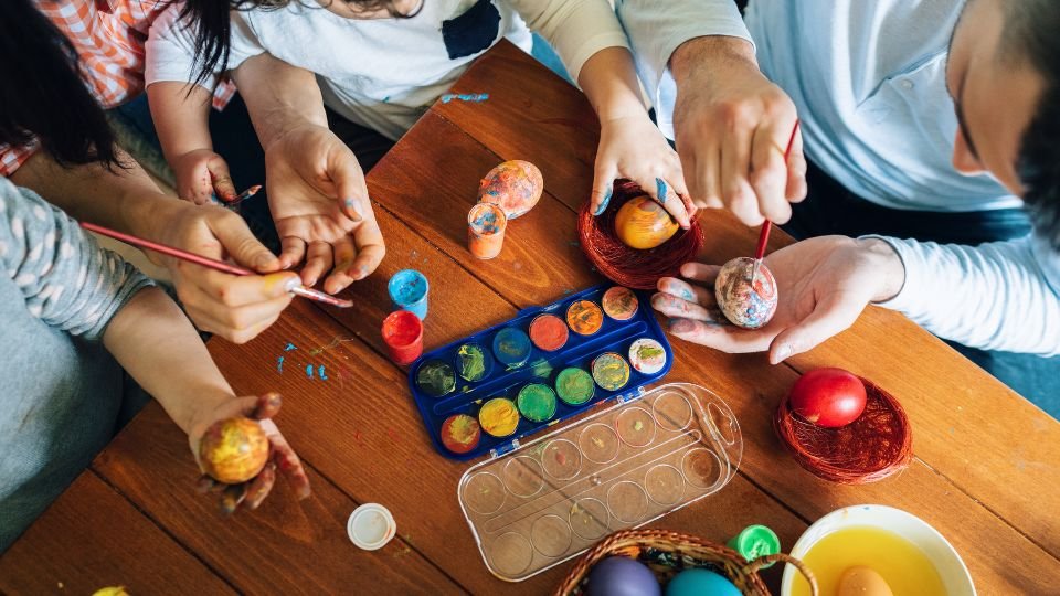 Családtagok tojásokat festenek színes festékekkel egy asztalon.