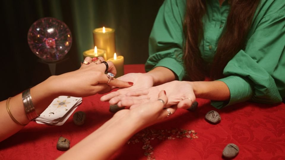 Tenyérjósról álmodni - jelentés és értelmezés Két nő tenyérjóslás közben, gyertyák és tarot kártyák mellett.