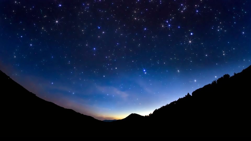 Csillagokkal teli égbolt, sötét hegyek sziluettjével a horizonton.