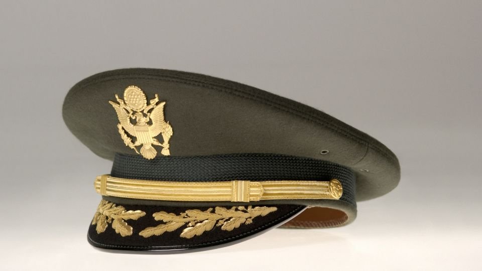 Egy ezredesi sapka, arany díszítéssel, szürke háttér előtt.