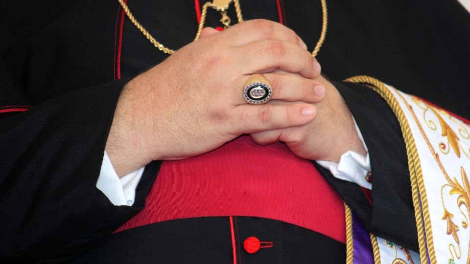 Egy érsek kezei, amelyeken látható a díszes gyűrű és a liturgikus öltözet.