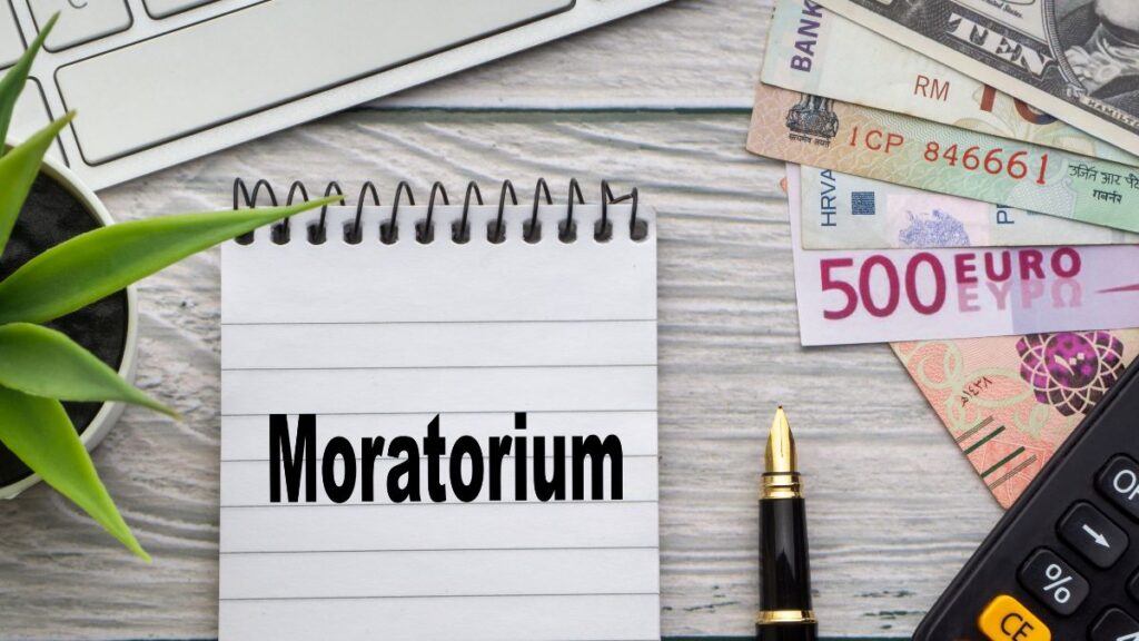Egy jegyzetfüzet, amelyen a 'Moratórium' felirat látható, pénz és toll mellett.