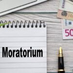 Egy jegyzetfüzet, amelyen a 'Moratórium' felirat látható, pénz és toll mellett.