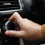 Egy kéz állítja az autóklíma hőmérsékletét, a műszerfalon.